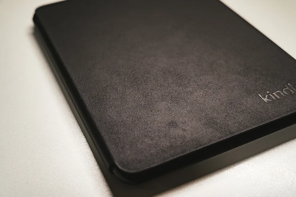 Amazon純正 植物性レザーカバー（ブラック）の外観を斜めから撮影。マットな質感と右下のkindleロゴ刻印が見える