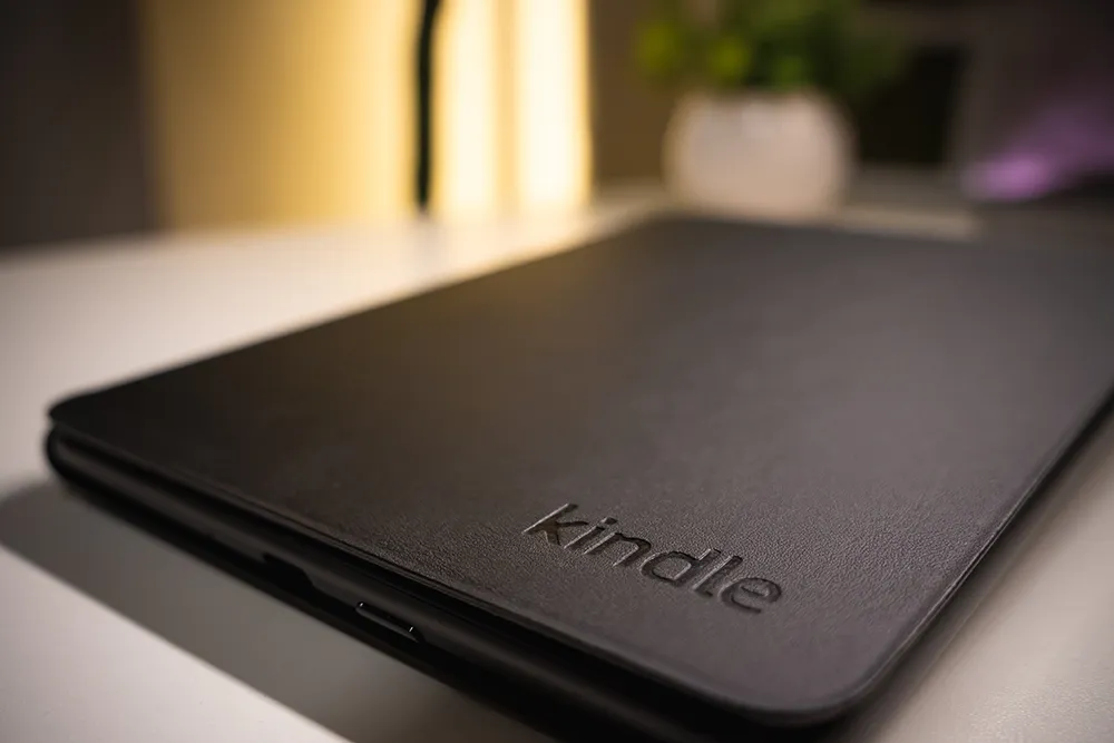 Amazon純正 植物性レザーカバーを装着したKindle Paperwhite。机上に置かれ、右下のkindleロゴが見える。実使用の雰囲気を伝える写真